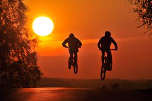 Rowerzyści wykonują skok w stronę zachodzącego słońca