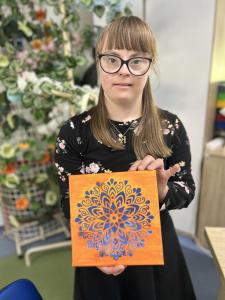 Uczestniczka trzyma pracę w formacie kwadratu - mandala wykonana za pomocą szablonu.