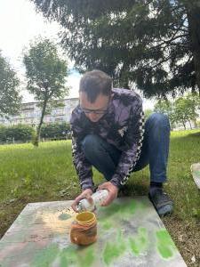 Uczestnik maluje sprayem kubek owinięty wełną. Prace wykonuje na otwartej przestrzeni.